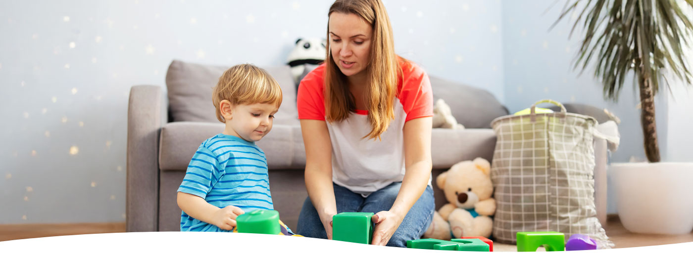 Eine Begleiter:In spielt mit einem Kind im Wohnzimmer